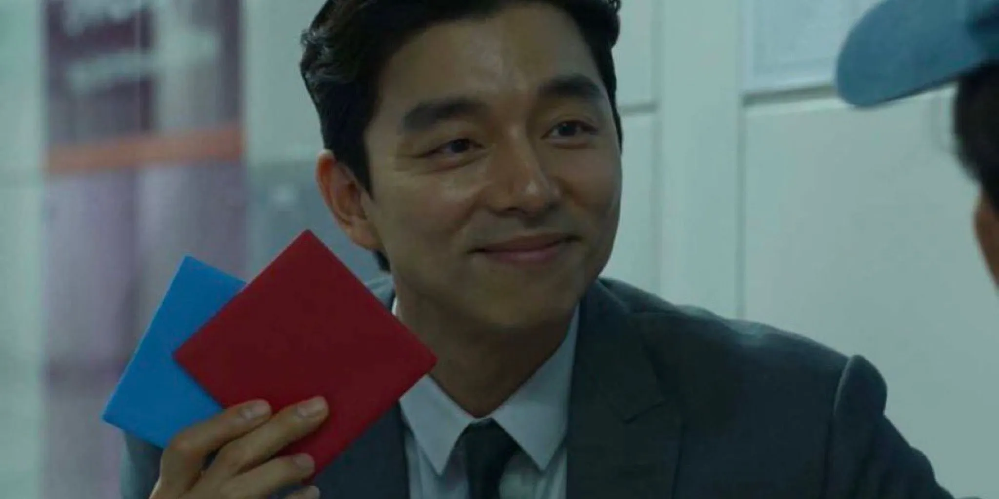 Gong Yoo در نقش فروشنده ای که کاشی قرمز Ddakji را در بازی Squid Game (2021) نگه می دارد